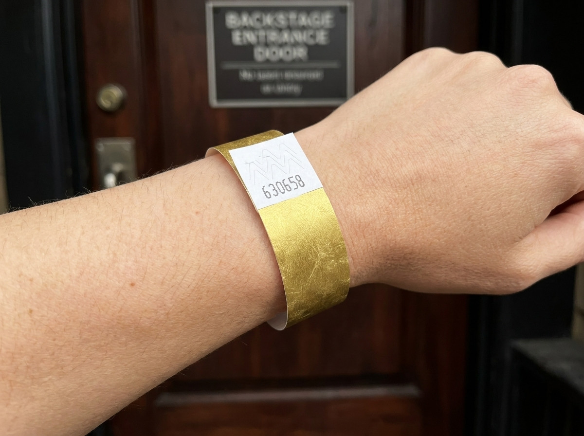 VIP-festivalarmband med guldmetallicktryck och streckkod, buret på ett handledd framför en backstageingång